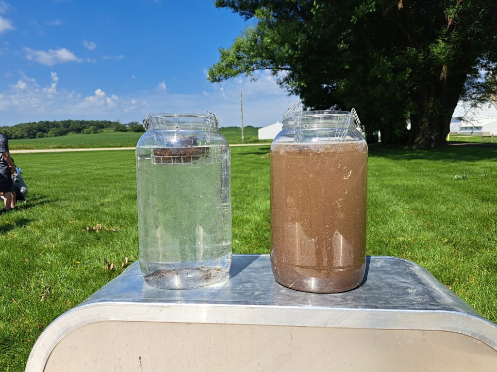 Visual of a slake test, two jars of water one is clear and one is filled with broken soil particles