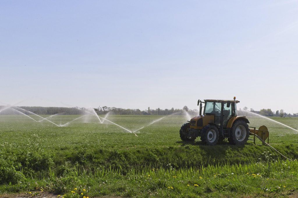 Tractor with irrigation equipment spraying water across green agricultural field.