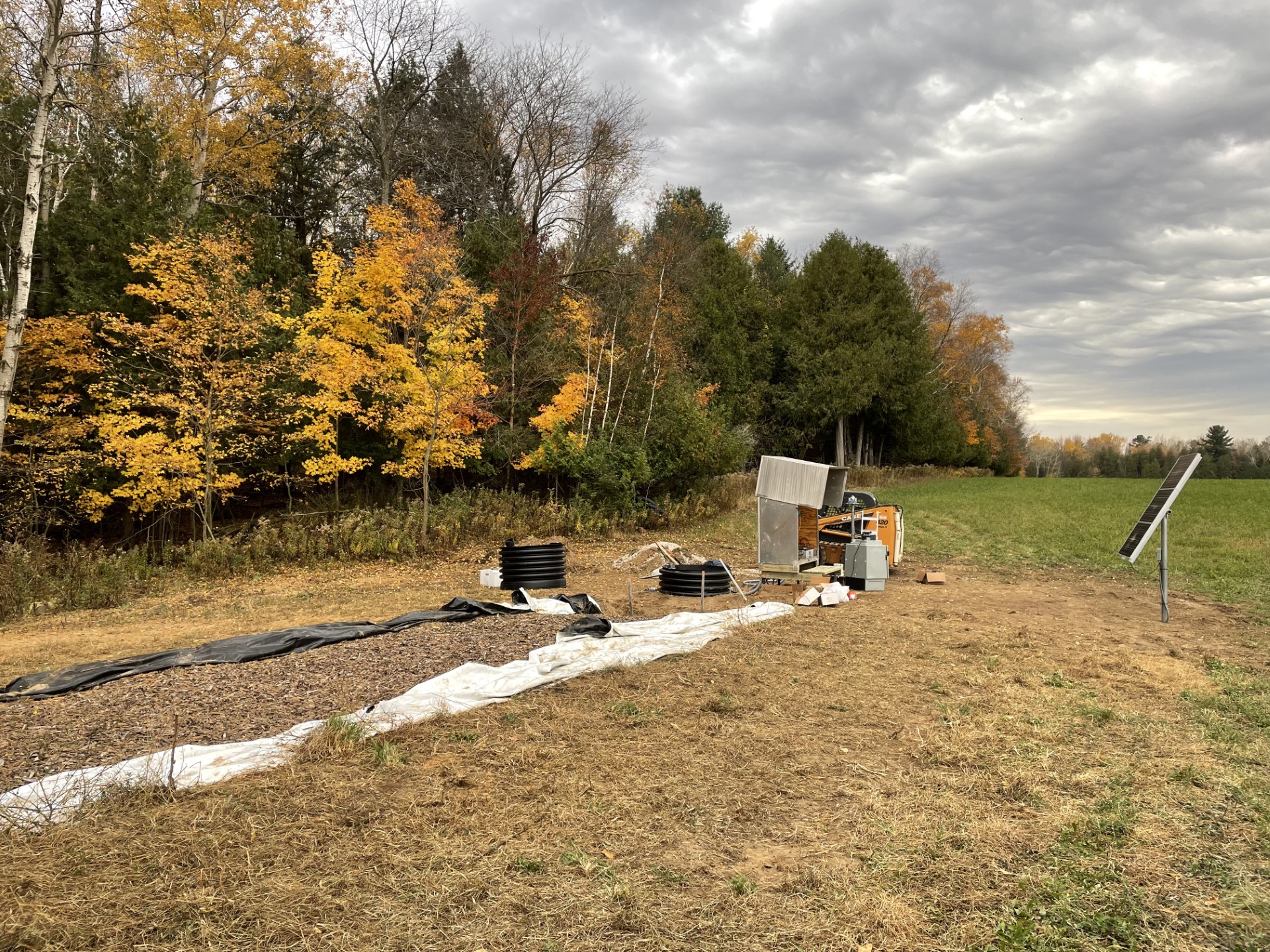 Bioreactor installation site with drainage pipes, monitoring equipment, and solar panel in agricultural field