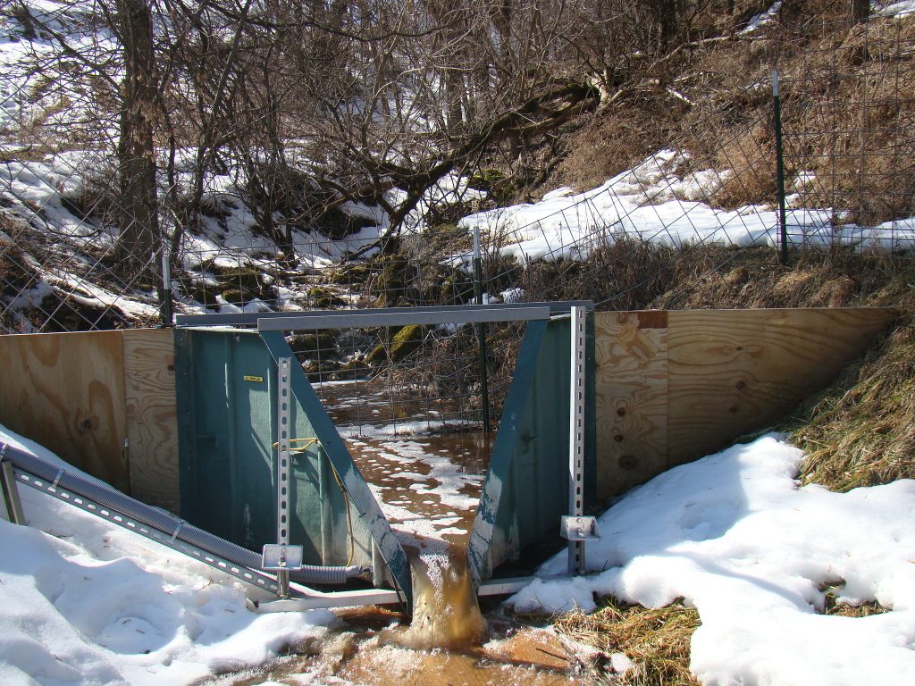 A metal research flume directing water in a snowy ravine.